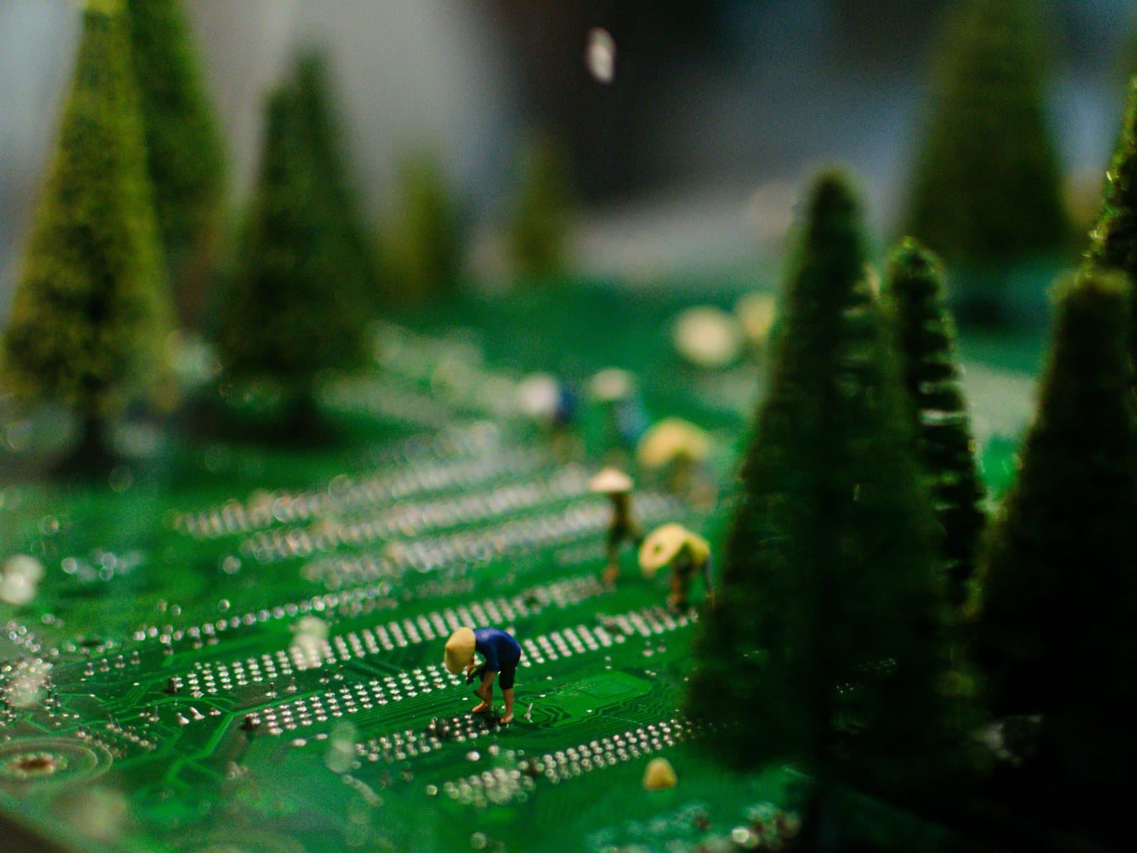 Miniature farmers tending rows of pine trees growing across a green circuit board