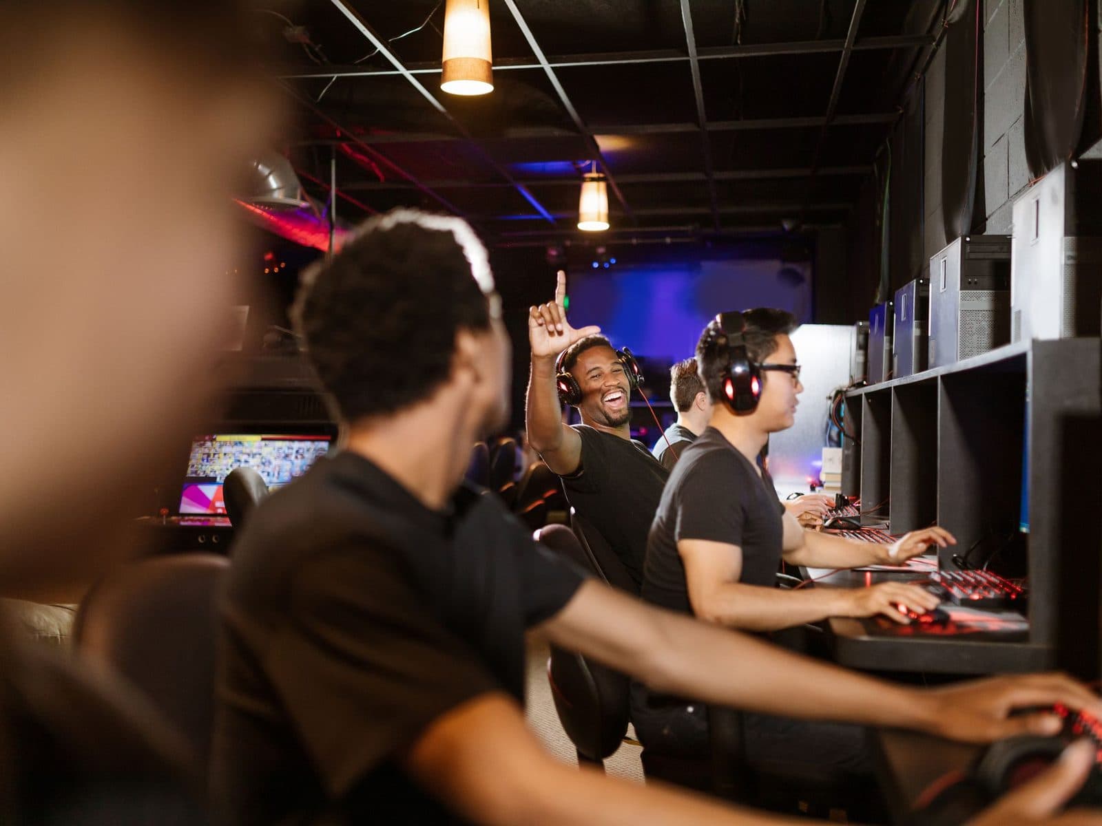 A row of people at computers under warm lamps, one arm in the air, everyone laughing